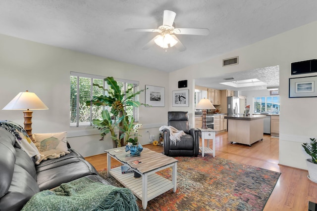 living room featuring ceiling fan, a textured ceiling, and light wood-type flooring