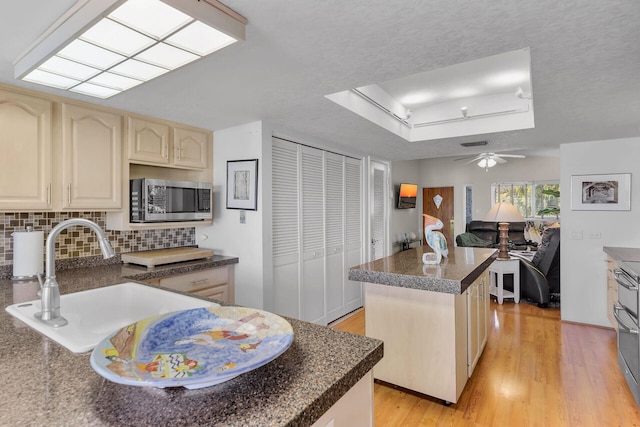 kitchen featuring sink, decorative backsplash, a center island, a tray ceiling, and light wood-type flooring