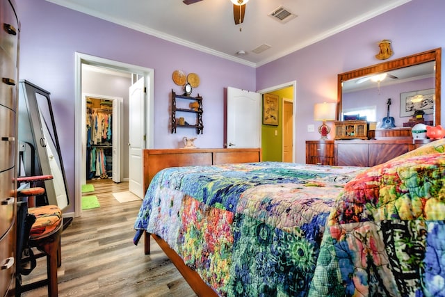 bedroom featuring a walk in closet, visible vents, crown molding, and wood finished floors