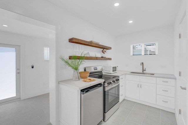 kitchen featuring sink, stainless steel range with electric cooktop, white cabinetry, light tile patterned floors, and dishwashing machine