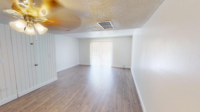 empty room featuring a textured ceiling, wood finished floors, visible vents, and baseboards