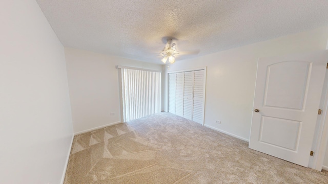 empty room with light carpet, a textured ceiling, a ceiling fan, and baseboards