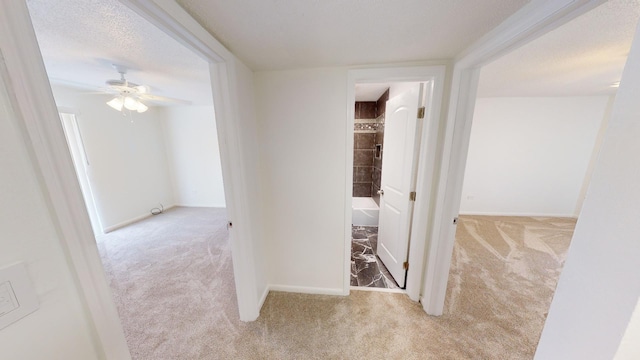 hall with a textured ceiling, baseboards, and carpet flooring