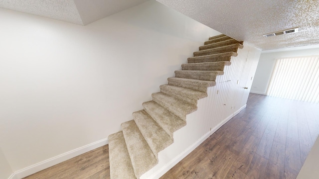 stairway featuring baseboards, a textured ceiling, visible vents, and wood finished floors