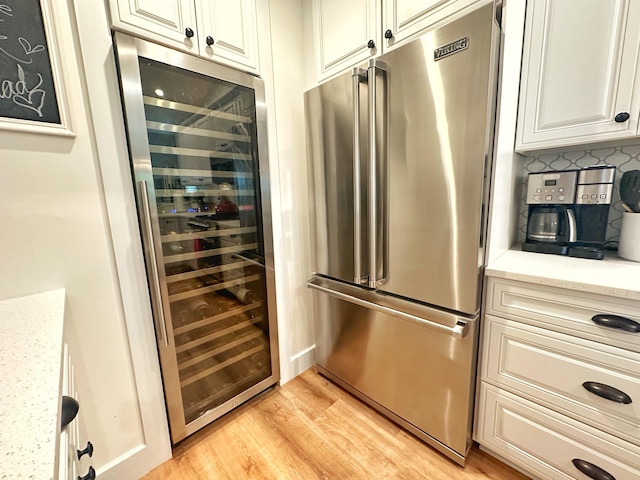 kitchen with backsplash, beverage cooler, light stone countertops, high end fridge, and light wood-type flooring