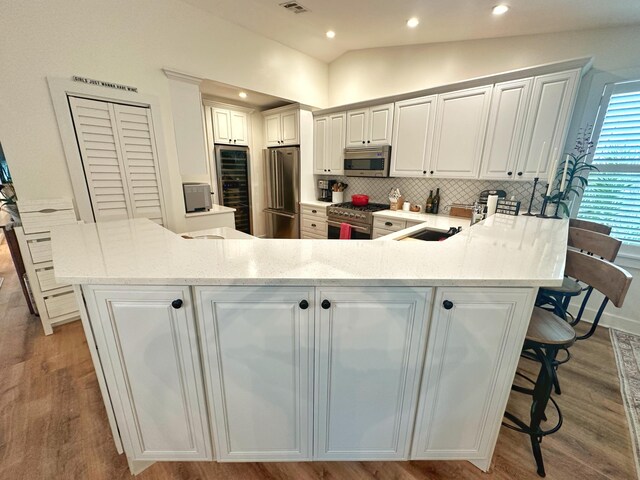 kitchen featuring a breakfast bar, white cabinetry, lofted ceiling, premium appliances, and kitchen peninsula