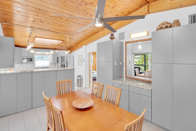 dining space featuring ceiling fan, lofted ceiling with skylight, light tile patterned floors, and wooden ceiling