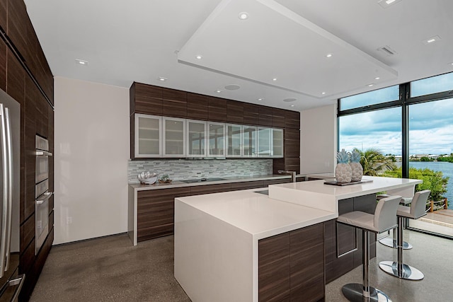 kitchen featuring a breakfast bar, a spacious island, expansive windows, black electric cooktop, and decorative backsplash