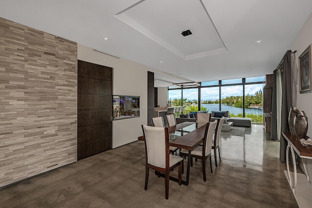 dining space with a tray ceiling, concrete flooring, expansive windows, and a water view