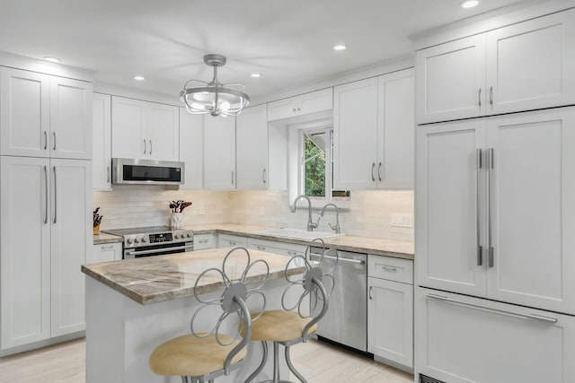 kitchen with appliances with stainless steel finishes, decorative light fixtures, sink, a center island, and light stone counters