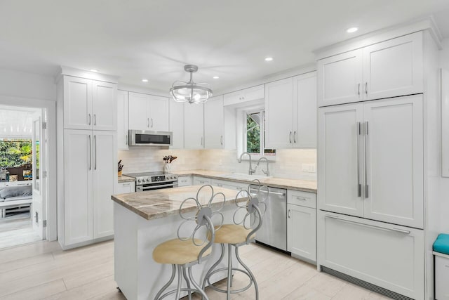 kitchen featuring stainless steel appliances, white cabinetry, a kitchen island, and sink