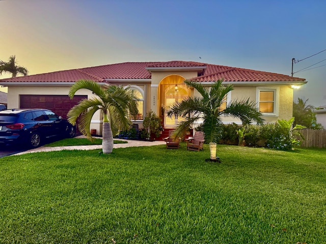 mediterranean / spanish-style house featuring a yard, stucco siding, a tiled roof, and an attached garage