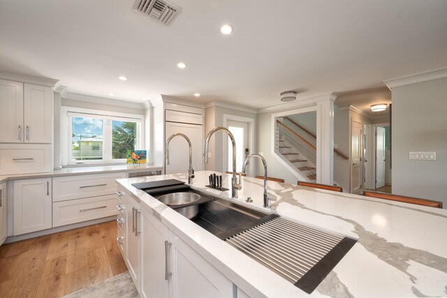 kitchen with ornamental molding, white cabinets, light stone counters, and light hardwood / wood-style floors