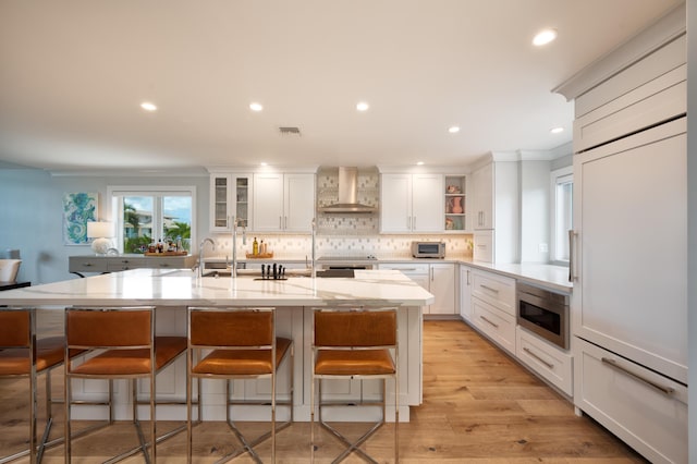 kitchen with stainless steel microwave, wall chimney range hood, light stone countertops, and white cabinets