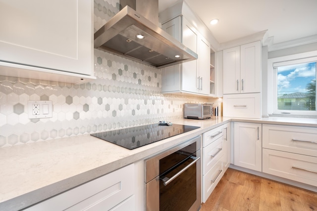 kitchen featuring black electric stovetop, white cabinets, exhaust hood, stainless steel oven, and light wood-type flooring