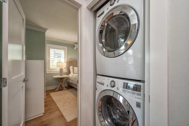 laundry room featuring stacked washer / drying machine, crown molding, and light hardwood / wood-style floors