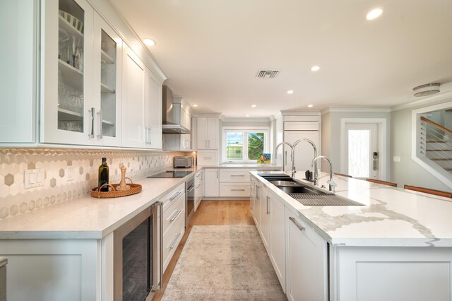 kitchen with white cabinets, beverage cooler, a kitchen island with sink, light stone countertops, and wall chimney exhaust hood