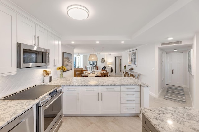 kitchen with stainless steel appliances, light stone countertops, white cabinets, and kitchen peninsula