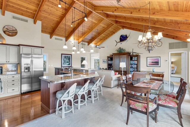 dining space with high vaulted ceiling, beamed ceiling, sink, a notable chandelier, and wooden ceiling