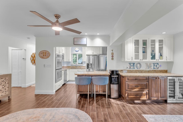 kitchen featuring a kitchen island, ceiling fan, stainless steel appliances, beverage cooler, and white cabinets