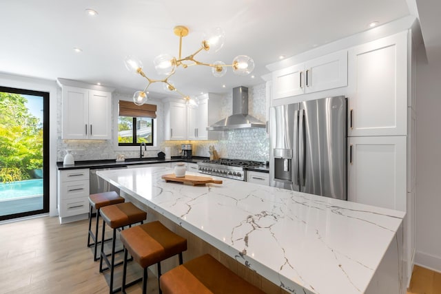 kitchen with wall chimney exhaust hood, sink, pendant lighting, stainless steel appliances, and white cabinets