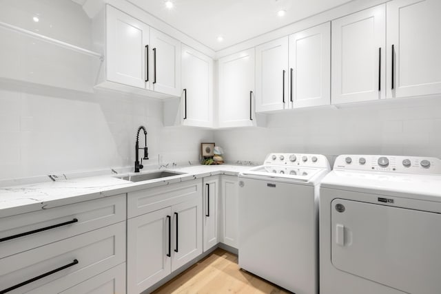 clothes washing area featuring separate washer and dryer, sink, light hardwood / wood-style flooring, and cabinets