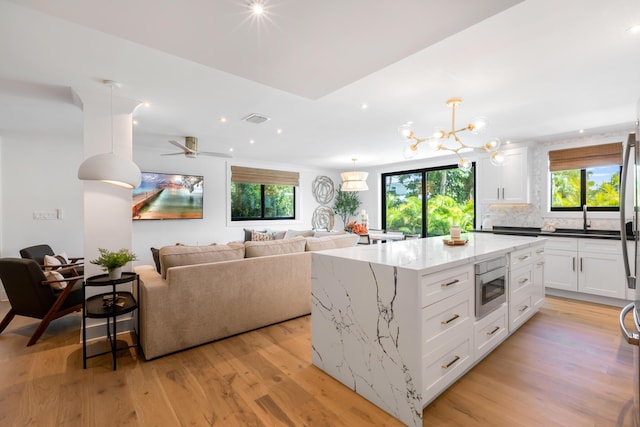 kitchen featuring stainless steel microwave, a kitchen island, dark stone counters, light hardwood / wood-style floors, and white cabinets