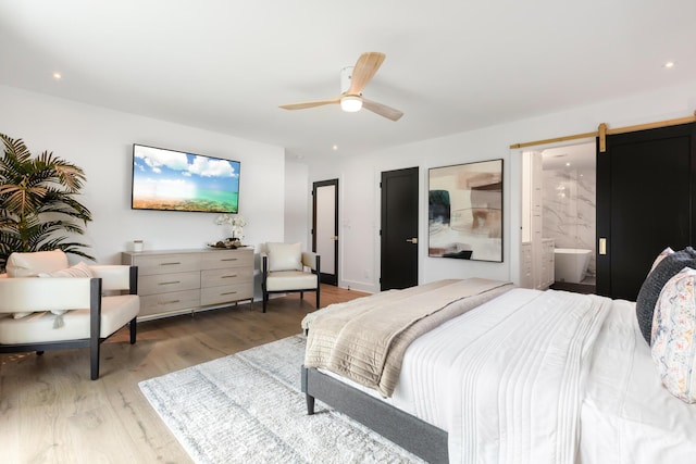 bedroom with ensuite bath, a barn door, ceiling fan, and light wood-type flooring