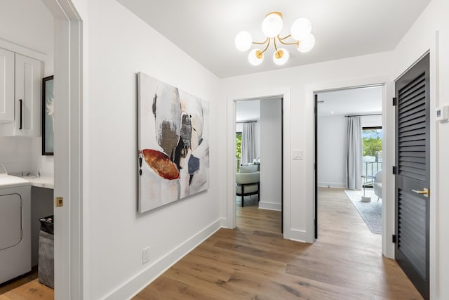 hall with a notable chandelier, washer / dryer, and light hardwood / wood-style flooring