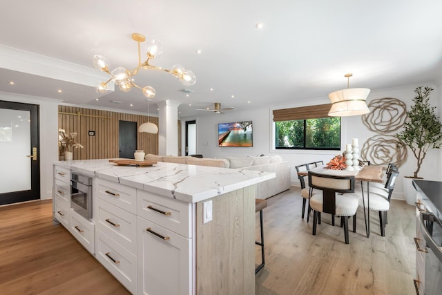 kitchen with a breakfast bar, white cabinetry, hanging light fixtures, light stone countertops, and a kitchen island