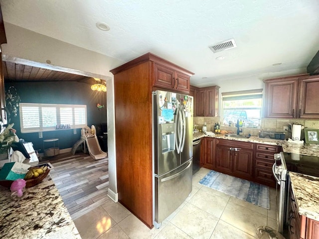 kitchen featuring sink, light tile patterned floors, appliances with stainless steel finishes, backsplash, and light stone counters