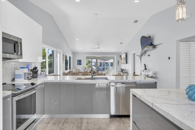 kitchen featuring vaulted ceiling, open floor plan, light stone countertops, modern cabinets, and appliances with stainless steel finishes