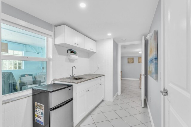 kitchen featuring light tile patterned floors, white cabinets, a sink, freestanding refrigerator, and light stone countertops
