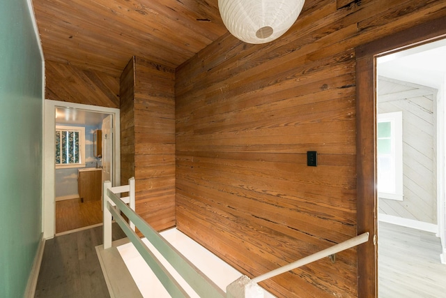 hallway with wooden walls, baseboards, wood finished floors, and an upstairs landing
