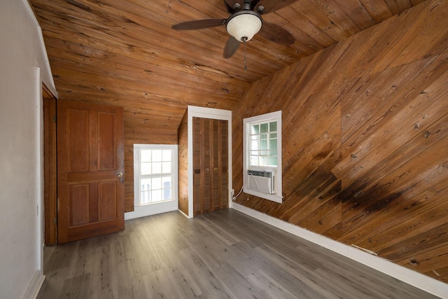 empty room with wood walls, lofted ceiling, wood finished floors, wooden ceiling, and a ceiling fan