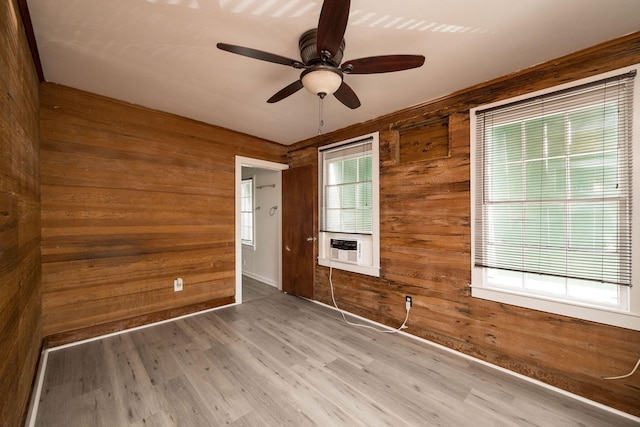 unfurnished room with plenty of natural light, wood walls, ceiling fan, and wood finished floors