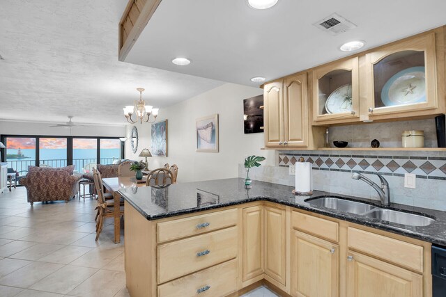 kitchen featuring sink, tasteful backsplash, kitchen peninsula, decorative light fixtures, and dark stone counters