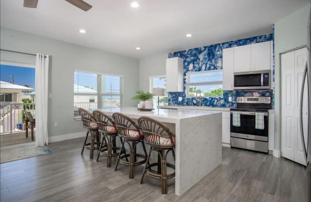 kitchen featuring a kitchen breakfast bar, dark hardwood / wood-style floors, stainless steel appliances, a center island, and white cabinets