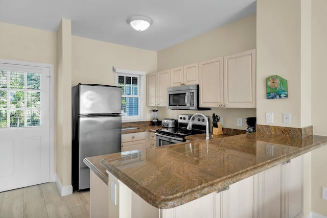 kitchen with a peninsula, appliances with stainless steel finishes, and dark stone countertops