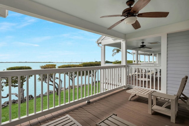 wooden deck with a water view, a ceiling fan, and a yard