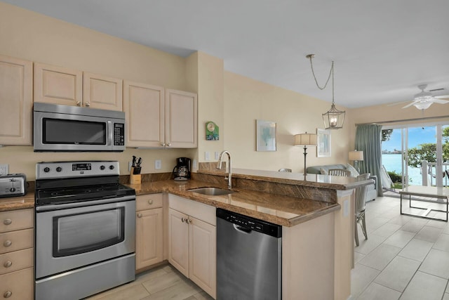 kitchen featuring open floor plan, a peninsula, stainless steel appliances, pendant lighting, and a sink