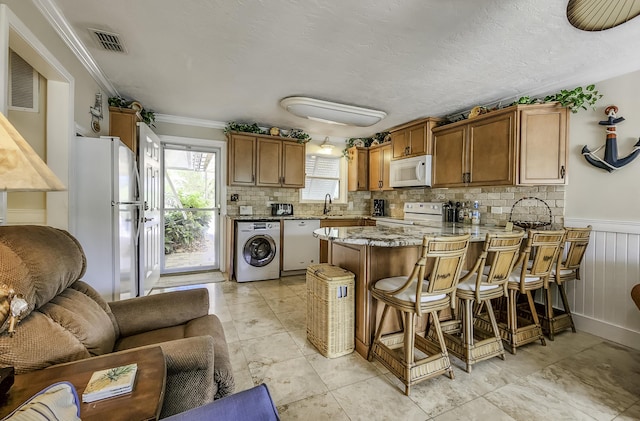 kitchen featuring washer / dryer, sink, a kitchen bar, kitchen peninsula, and white appliances