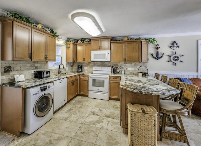 kitchen featuring sink, white appliances, a breakfast bar, light stone countertops, and washer / dryer