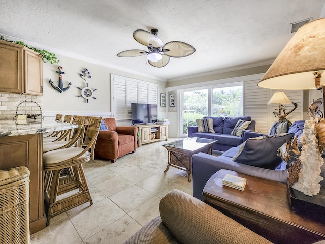 tiled living room with ceiling fan, ornamental molding, and a textured ceiling