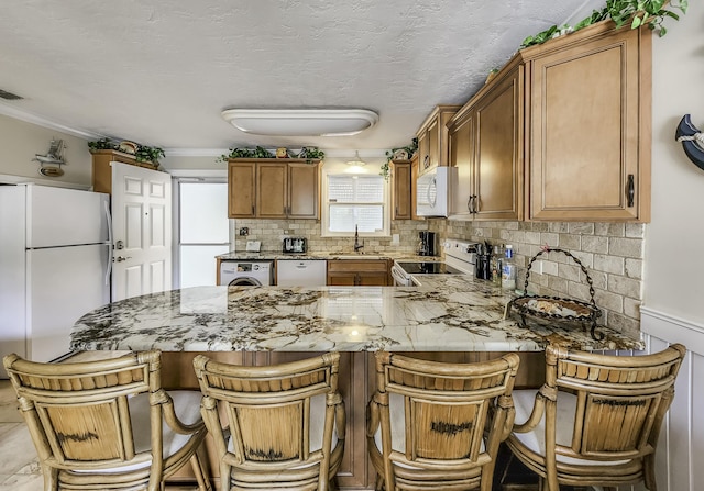 kitchen featuring sink, a breakfast bar area, backsplash, kitchen peninsula, and white appliances