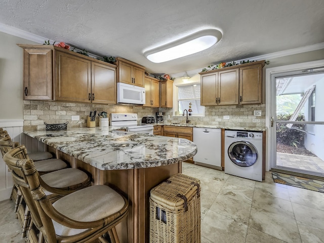 kitchen featuring washer / clothes dryer, sink, a breakfast bar area, kitchen peninsula, and white appliances