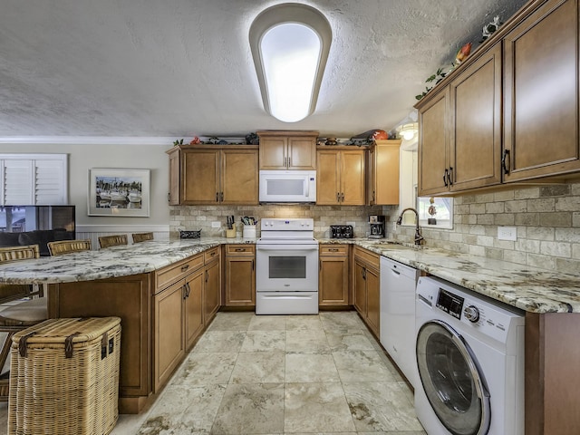 kitchen featuring white appliances, a breakfast bar, light stone countertops, washer / clothes dryer, and kitchen peninsula