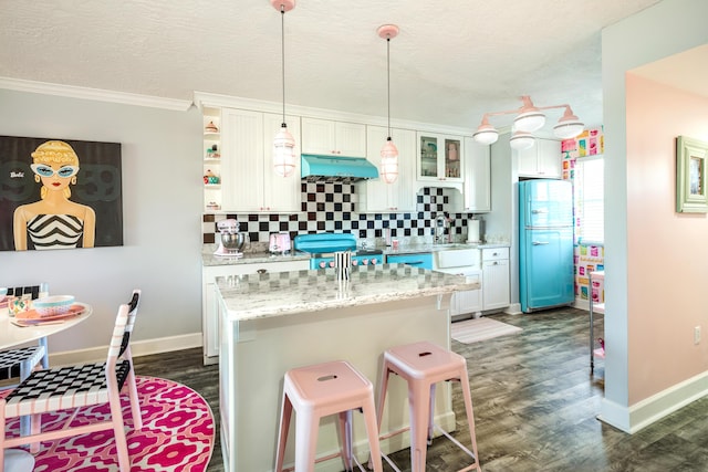 kitchen with white cabinetry, light stone counters, decorative light fixtures, refrigerator, and a kitchen island