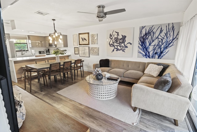 living room featuring ceiling fan with notable chandelier, wood finished floors, visible vents, and baseboards