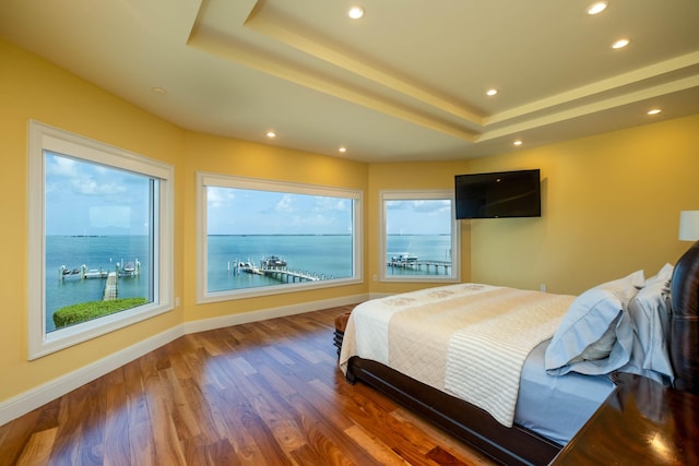 bedroom featuring a water view, wood-type flooring, and a tray ceiling